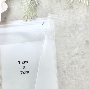 May include: Clear plastic bags with measurements printed on them. The bags are 7 cm by 7 cm.