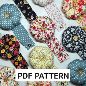 Puede incluir: Una colección de nueve alfileteros con diferentes patrones de tela. Los alfileteros tienen forma de flor y tienen un botón en el centro. Los alfileteros están unidos a tiras de tela con diferentes patrones. El texto "PDF PATTERN" se muestra en la parte inferior de la imagen.