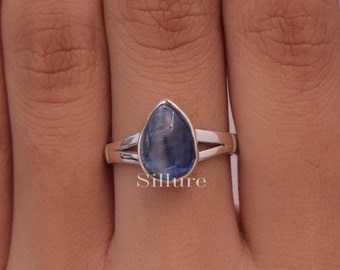 May include: A silver ring with a teardrop-shaped blue gemstone. The ring is set with a split shank and has a simple design.