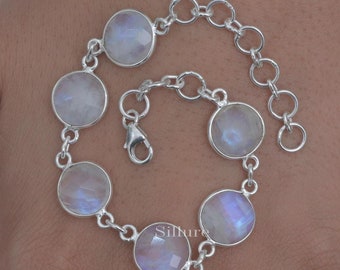 May include: A silver bracelet featuring seven round, faceted moonstone cabochons. The stones are set in individual bezels and connected by small silver links. The bracelet has a lobster clasp closure and an adjustable chain.