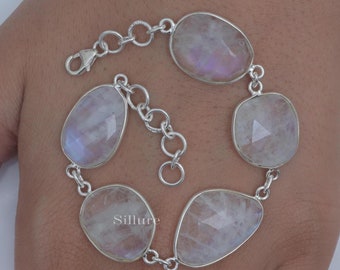 May include: A silver bracelet featuring six iridescent moonstone cabochons. The stones are set in a silver chain with a lobster clasp closure. The moonstones have a soft, pearly sheen.