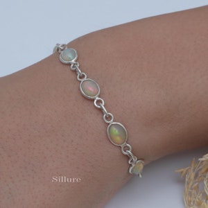 Puede incluir: Un brazalete de cadena de plata con cinco piedras de ópalo de forma ovalada. El brazalete está en la muñeca de una persona.