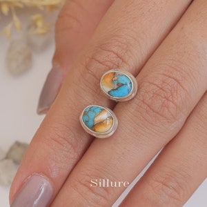 Peut inclure: Une paire de boucles d'oreilles à clous ovales. Chaque boucle d'oreille présente une pierre turquoise et orange sertie dans une lunette en argent. Les boucles d'oreilles sont présentées sur un fond clair.