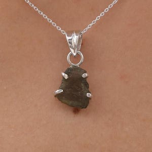 May include: A silver chain necklace with a pendant featuring a dark green, irregularly shaped stone set in a silver frame.