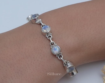 May include: A silver chain bracelet featuring four round, bezel-set moonstones with a blue iridescent sheen. The links are connected by small silver rings, and the word Sillure is printed in small white text near the bottom of the bracelet.