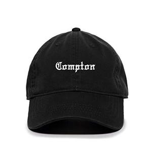 May include: Black baseball cap with white embroidered text that reads "Compton" in old English font.