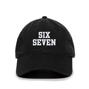 May include: Black baseball cap with the text "SIX SEVEN" in white block letters. The cap has a curved brim and a rounded crown. A casual accessory for everyday wear.