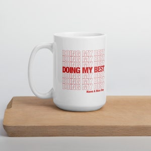 May include: White ceramic mug with a red graphic that says "DOING MY BEST" repeated multiple times. The text is outlined in white. The text "Have A Nice Day" is printed in smaller font below the graphic.
