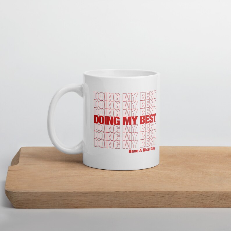 May include: White ceramic mug with the text "DOING MY BEST" repeated in red, stacked on top of each other. The text "Have A Nice Day" is printed in red at the bottom of the mug.