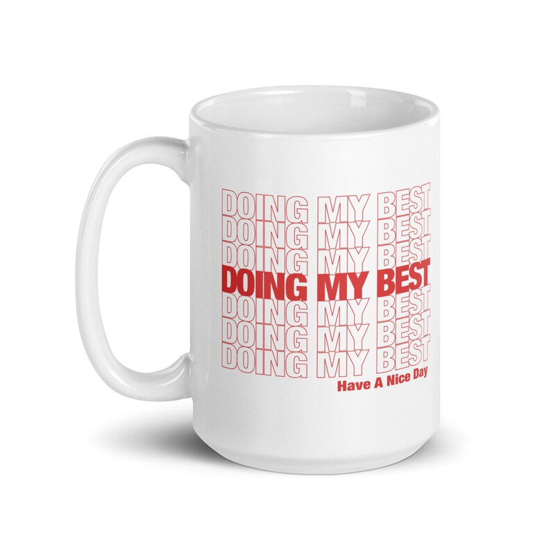 May include: White ceramic mug with a red graphic that says "DOING MY BEST" repeated multiple times. The text is in a stacked, staggered pattern. The bottom of the mug says "Have A Nice Day".