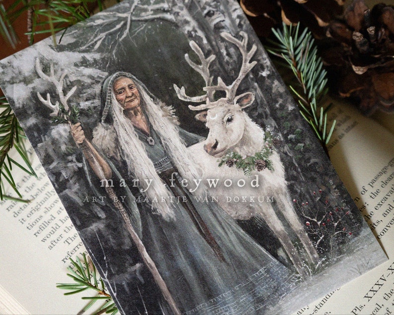 May include: A rectangular art print featuring an illustration of an elderly person with long white hair wearing a dark hooded cloak and holding a wooden staff, standing beside a white reindeer with a wreath, with text reading mary feywood art by maartje van dokkum.