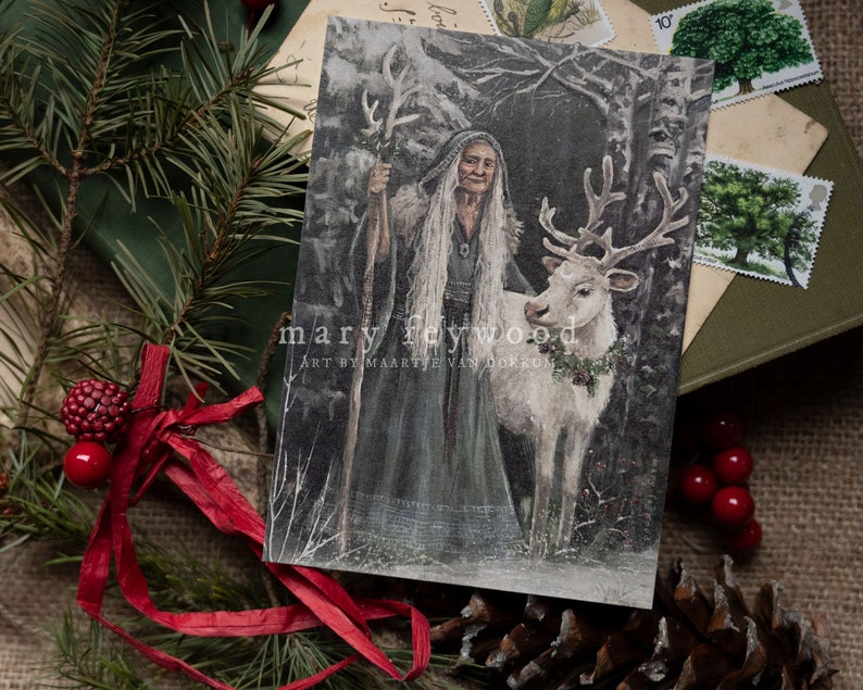 May include: A rectangular art print featuring an elderly person with long white hair wearing a dark hooded cloak and holding a staff, standing beside a white reindeer with a wreath around its neck. The text reads mary feywood ART BY MAARTJE VAN DORKUM.