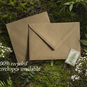 May include: Two brown paper envelopes with a green fern stamp on one of them. The envelopes are lying on a bed of green moss and white flowers. The text "100% recycled envelopes available" is printed below the envelopes.