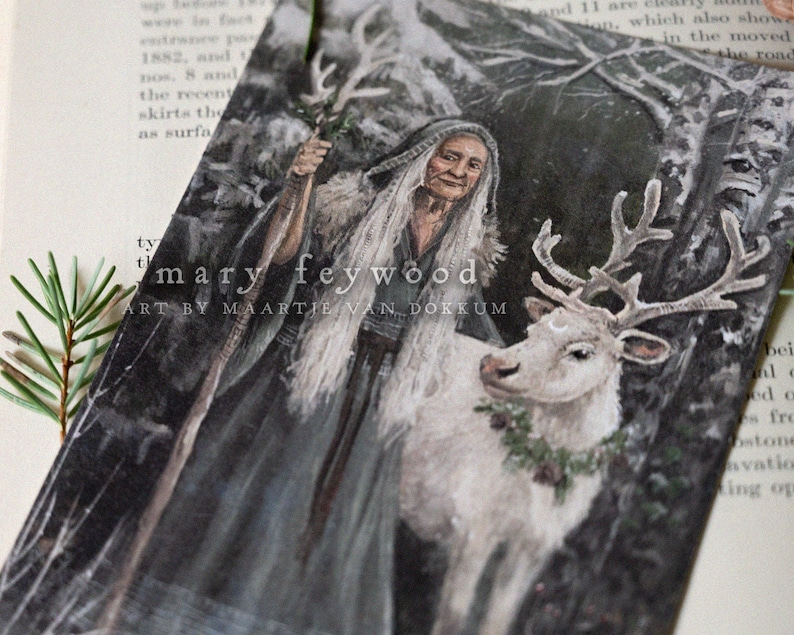 May include: A rectangular art print featuring a painting of an elderly person with long white hair wearing a dark hooded cloak and holding a staff, standing next to a white reindeer with antlers and a green wreath. Text reads mary feywood.