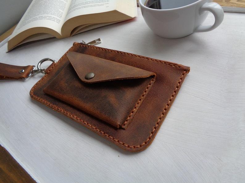 May include: A brown leather pouch with a zipper closure and a smaller flap pocket. The pouch has a strap with a metal ring.