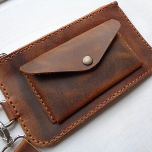 May include: A brown leather wallet with a zipper closure and a flap pocket. The wallet has a silver snap closure and a metal ring.