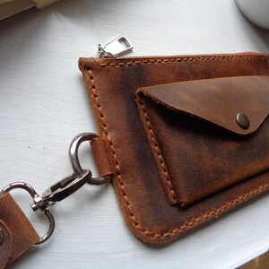 May include: A brown leather wallet with a zipper closure and a small flap pocket. The wallet has a metal clasp and a strap.