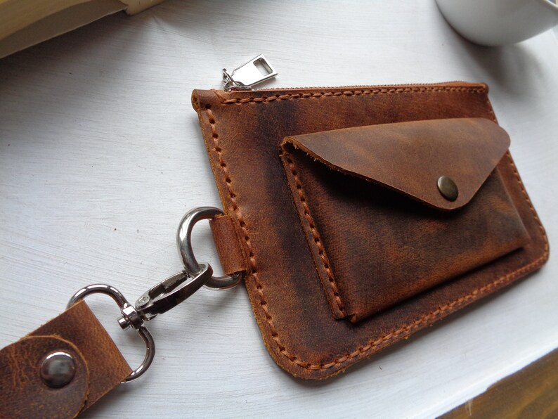 May include: A brown leather wallet with a zipper closure and a small flap pocket. The wallet has a metal clasp and a strap.