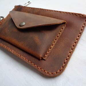 May include: A brown leather wallet with a flap closure and a zippered pocket. The wallet has a distressed look and is stitched with brown thread.