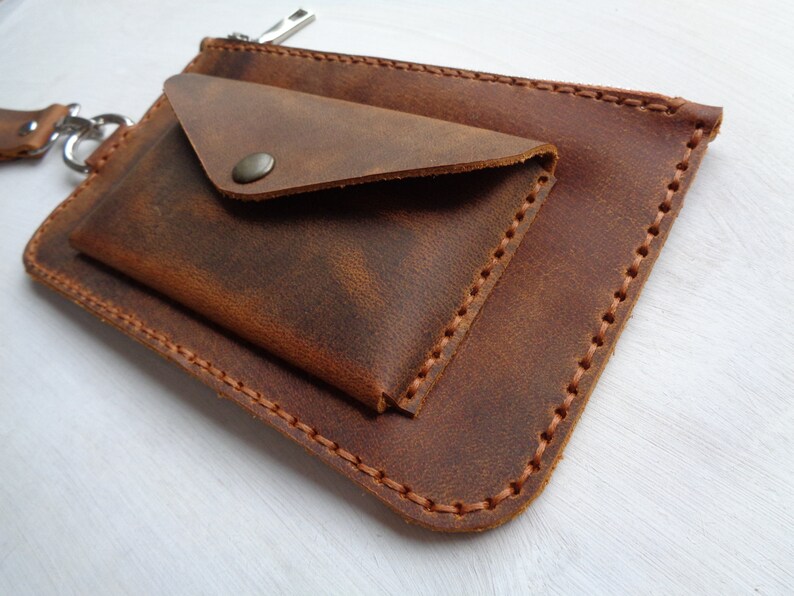 May include: A brown leather wallet with a flap closure and a zippered pocket. The wallet has a distressed look and is stitched with brown thread.