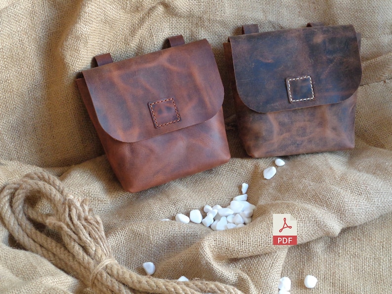 Peut inclure: Deux sacs en cuir marron avec des fermetures &agrave; rabat et des d&eacute;tails cousus. Les sacs sont pos&eacute;s sur une surface en toile de jute avec des pierres blanches.