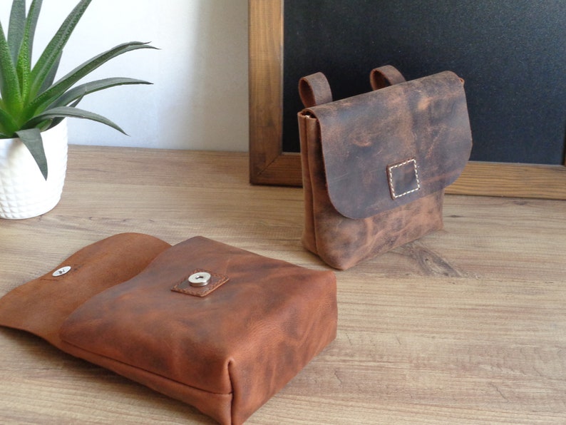Peut inclure: Deux sacs en cuir marron avec une fermeture &agrave; rabat et un bouton pression. Le sac de gauche est ouvert, montrant l'int&eacute;rieur. Le sac de droite a une sangle.