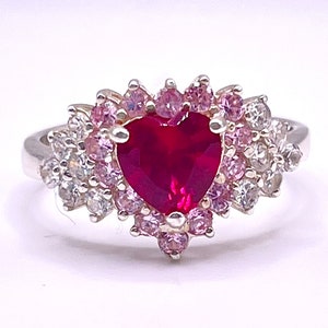 May include: A silver ring with a large heart-shaped ruby surrounded by smaller pink and white stones.