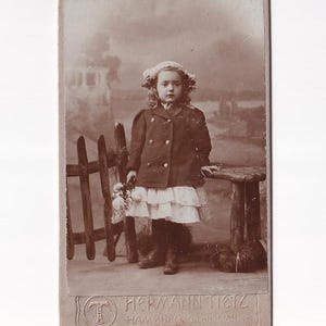 Mädchen mit Haube und doppelreihiger Jacke vor Landschaftskulisse, deutsches Visitfoto (Hermann Tietz, Hamburg)