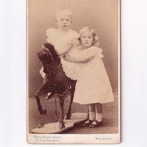 Chłopiec jadący na dużym koniu-zabawce obok dziewczynki, zdjęcie z wizyty w Niemczech (Franz Radmacher, Fritz Küken Nachfolger, Bielefeld)