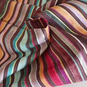 Puede incluir: Tela de rayas multicolores con un patr&oacute;n ondulado. La tela est&aacute; hecha de un material suave y texturizado y presenta una variedad de colores, incluyendo marr&oacute;n, naranja, azul verdoso, rosa y morado.