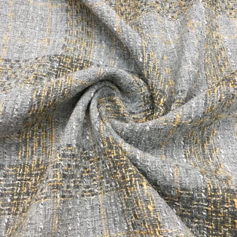 K&ouml;nnte beinhalten: Nahaufnahme eines grauen und gelben Tweed-Stoffes mit gewebter Struktur. Der Stoff ist weich und hat einen dezenten Glanz.