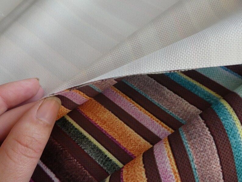 Puede incluir: Primer plano de dos muestras de tela, una blanca y otra con rayas de colores. La tela blanca est&aacute; doblada sobre la tela rayada, revelando la textura de ambas telas.