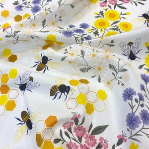 Puede incluir: Tela blanca con un patrón repetido de panales de miel amarillos y marrones, abejas y flores rosas, amarillas y moradas.