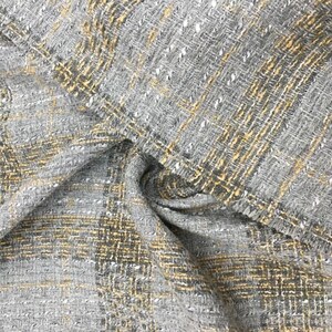 K&ouml;nnte beinhalten: Nahaufnahme eines grauen und gelben Tweed-Stoffes mit gewebter Textur. Der Stoff hat einen dezenten Glanz und ein leicht raues Gef&uuml;hl.