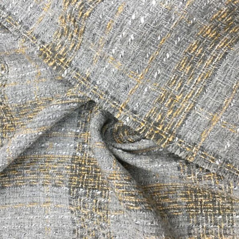 K&ouml;nnte beinhalten: Nahaufnahme eines grauen und gelben Tweed-Stoffes mit gewebter Textur. Der Stoff hat einen dezenten Glanz und ein leicht raues Gef&uuml;hl.