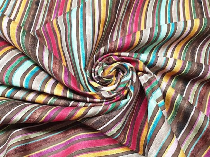 Puede incluir: Tela rayada multicolor sobre fondo marr&oacute;n. La tela est&aacute; doblada y retorcida, mostrando los diferentes colores y patrones.