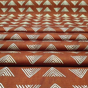 May include: Close-up of a folded fabric with a repeating pattern of white chevron shapes on a rust-colored background.