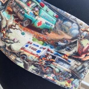 May include: A colorful fabric headband with a repeating pattern of Winnie the Pooh characters and ambulances. The headband features a green and white ambulance with the text "Ambulance Squad 57" and a red cross.