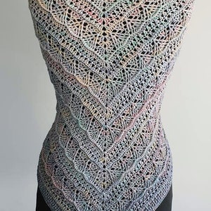 Puede incluir: Un chal de ganchillo triangular con un hilo multicolor en tonos azules, verdes, rosas y amarillos. El chal se muestra en un maniquí negro.