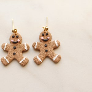 May include: A pair of gingerbread man earrings with white icing and black eyes. The earrings are made of polymer clay and have gold hooks.
