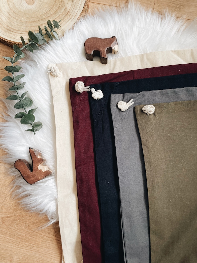 Puede incluir: Un conjunto de seis cuadrados de tela en varios colores, incluyendo beige, burdeos, negro, gris y verde oliva. Cada cuadrado tiene un detalle de cuerda anudada en la esquina.