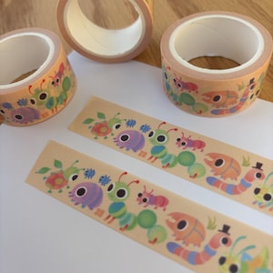 Puede incluir: Rollos y tiras de cinta washi decorativa con un diseño de insectos coloridos. La cinta tiene un fondo marrón claro con ilustraciones de varios insectos en tonos verdes, morados, naranjas y azules. Ideal para manualidades y scrapbooking.