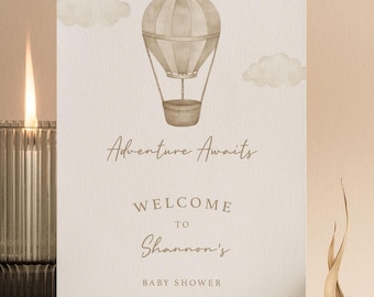 May include: A white rectangular card featuring a watercolor illustration of a beige hot air balloon and clouds. The text reads: Adventure Awaits, WELCOME TO Shannon's BABY SHOWER, 01.09.24. The card has a textured paper finish.