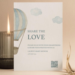 May include: A white card with a blue and white hot air balloon illustration. The card says "Share the Love" and has a QR code. The text below the QR code says "Please scan with your smartphone & share your photos with us Lauryn's Baby Shower 27th May 2013". The bottom of the card says "Full & Love".