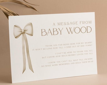 May include: A white card with a brown bow and the text "A message from Baby Wood" and a message from the baby to their guests. The card is on a light brown surface with a white candle.