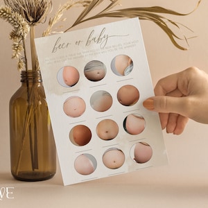 May include: A white card with the text "Beer or Baby" printed on it. The card has 16 circles with photos of pregnant bellies inside each circle. The card is being held by a hand.