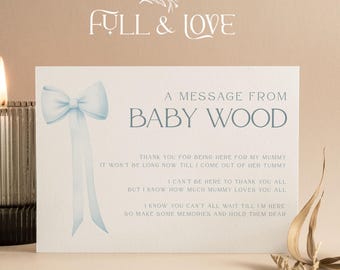 May include: A lit candle in a ribbed glass holder sits next to a card with a blue bow illustration and the text "A MESSAGE FROM BABY WOOD". The card has a message about a baby. The background is a soft beige.