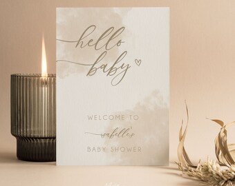 May include: A rectangular white card with beige watercolor accents featuring the text hello baby with a small heart, followed by the text WELCOME TO Isabelle's BABY SHOWER in a mix of script and sans-serif fonts, displayed upright.