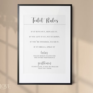 May include: A black framed print with white text that reads "Toilet Rules" and includes a list of rules for using the restroom. The rules include "If it runs out, replace it", "If you lift it up, put it down", "If you're finished, flush it", "If it smells, spray it", "Ladies, please remain seated for the entire performance", and "Gentlemen, stand close, it may be smaller than you think".