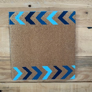 May include: A corkboard with a blue and light blue chevron border. The corkboard is a rectangular shape and is made of natural cork.